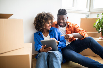 Fototapeta na wymiar Smiling Black Spouses Using Digital Tablet While Relocating To New Apartment