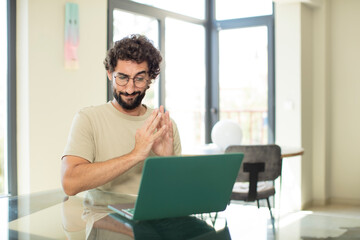 young adult bearded man with a laptop feeling proud, mischievous and arrogant while scheming an evil plan or thinking of a trick