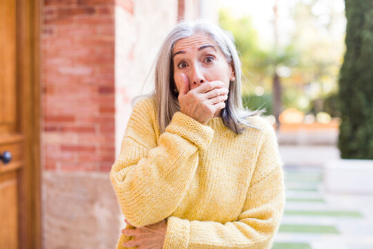 senior retired pretty white hair woman covering mouth with hands with a shocked, surprised expression, keeping a secret or saying oops