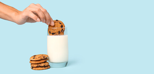 Woman dipping tasty cookie in glass of milk on light blue background with space for text