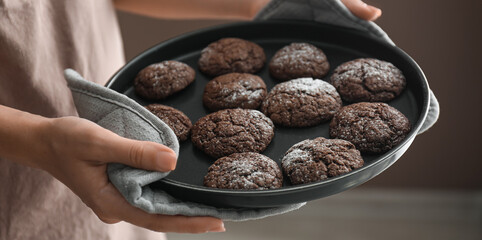Woman holding baking tray with chocolate cookies, closeup