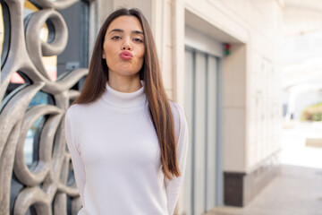 pretty young adult woman pressing lips together with a cute, fun, happy, lovely expression, sending a kiss
