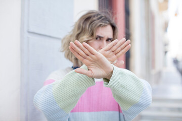 pretty woman covering face with hand and putting other hand up front to stop camera, refusing...