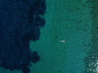 Above view of woman swimming at sea. Aerial top view of young girl in white swimsuit floating on...