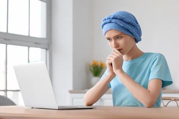 Teenage girl after chemotherapy using laptop at table in kitchen