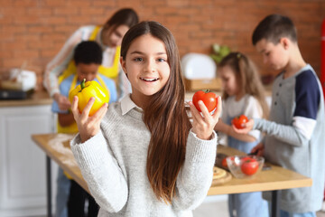 Little girl with vegetables during cooking class in kitchen