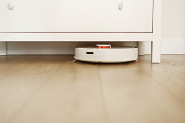 Wireless autonomous robotic vacuum cleaner vacuums with brushes under commode at living room. Self-propelled cleaning robot. Household remote control appliances. Smart cleaning technology.