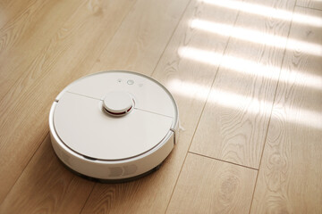 Top view of white wireless autonomous robotic vacuum cleaner on wooden floor. Smart cleaning...