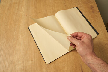 A white male hand turning the blank pages of a diary, notebook.