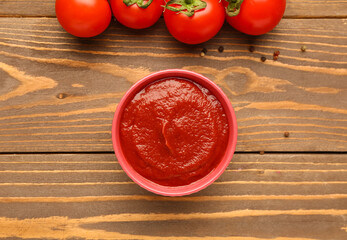 Bowl with tasty tomato paste on wooden background