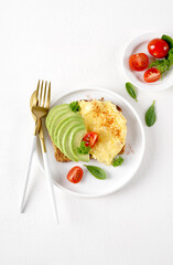 Omelette with tomato and avocado on bread on white plate, light background, vertical top view
