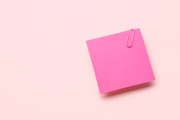 Pink sticky note with paper clip on color background