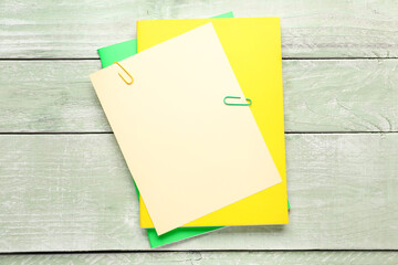 Beige, yellow and green paper sheets with clip on color wooden background