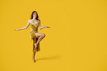 Fototapeta na wymiar Full length shot of fashionable lady in golden elegant dress posing on yellow studio background, free space