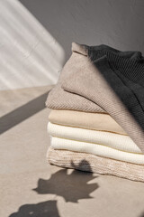 Stack of beige, taupe, white, light brown knitted sweaters on neutral beige background with...