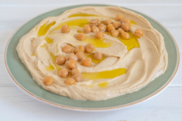 Chickpeas and olive oil over freshly prepared hummus in ceramic plate.