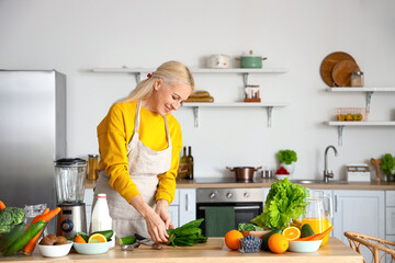Mature woman with fresh vegetables and fruits making healthy smoothie in kitchen