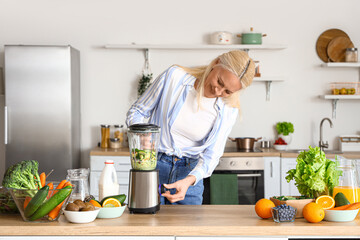 Mature woman making healthy smoothie with blender in kitchen
