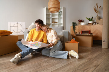 Young couple with house plan sitting in room on moving day - obrazy, fototapety, plakaty