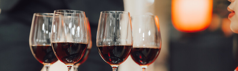 Low angle close up perspective of crystal clear wine glass with traditional round goblet shape filled with dark red wine and slim stem on wood counter top bar with blurry restaurant background scene