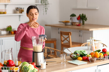 Sporty young woman making healthy smoothie with blueberries in kitchen