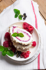 Meringue roll with whipped cream and currant curd, served with berries on a ceramic plate. Rustic style.