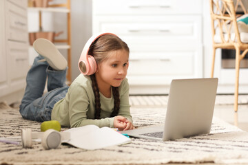 Little girl in headphones with laptop studying computer sciences online at home