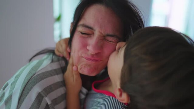 Energetic child kissing mother in cheek with rough embrace. Excited son warm loving embrace kisses mom energetically