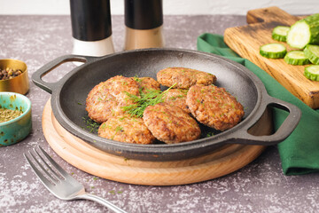 Frying pan with cutlets, dill and wooden board on grey grunge table in kitchen