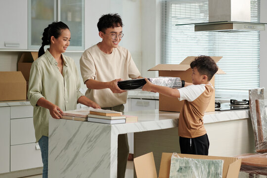 Cheerful parents asking son to put wrapped pictures in cardboard boxes