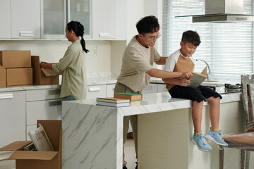 Smiling father giving book his preteen son sitting on kitchn island