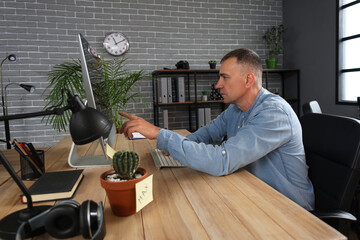 Mature male programmer pointing at computer monitor with programming code in office