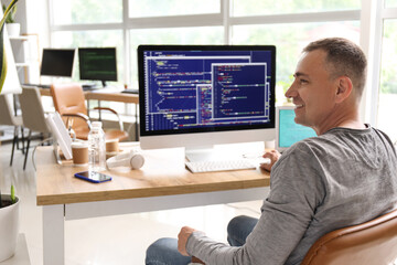 Mature male programmer sitting in light office at his workplace