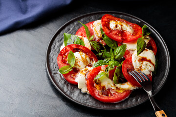 Caprese Salad. Tomato and mozzarella slices with basil leaves with fork on dark plate. Traditional Italian food