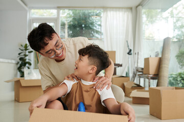 Father and son sitting in carboard box playing together at home