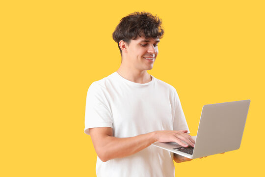 Male programmer working with laptop on yellow background