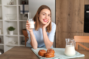 Young woman with glass of milk and tasty buns in kitchen