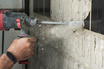 Builder with a puncher dismantles old tiles from a concrete wall