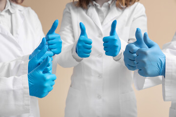 Doctors in medical gloves showing thumbs-up on beige background, closeup