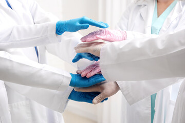 Doctors in medical gloves putting hands together at clinic, closeup