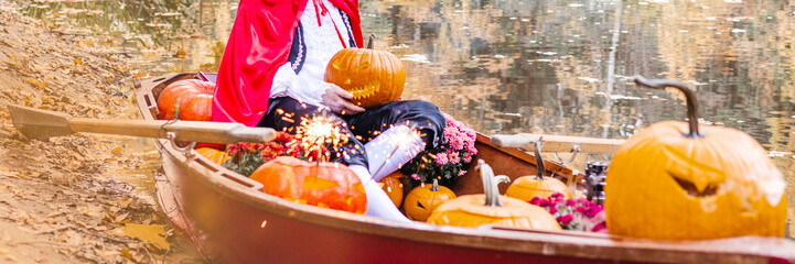 banner young man dressed as gondolier in gondola boat decorated with pumpkins on pond in autumn park celebrates Halloween and having fun, concept of Halloween carnival or costume party