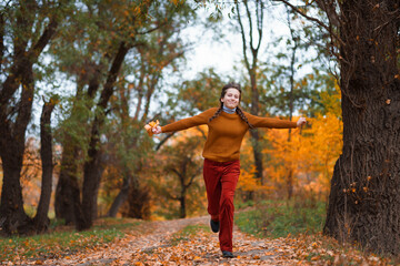 a young teenage girl runs through the autumn forest along a dirt road and enjoys the beautiful nature and bright yellow leaves