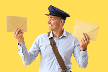 Mature postman with envelopes on yellow background