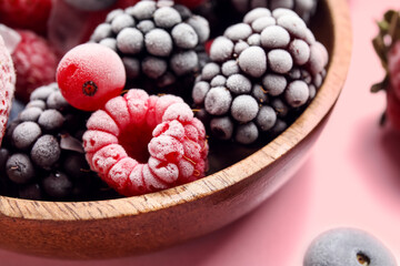 Bowl of frozen berries on pink background, closeup