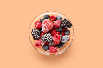 Glass bowl of frozen berries on color background