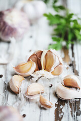 Closeup of Red Inchelium garlic cloves on white wooden table with garlic bulbs in background. Selective focus with blurred foreground and background.
