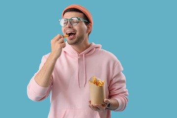 Young man eating french fries on blue background