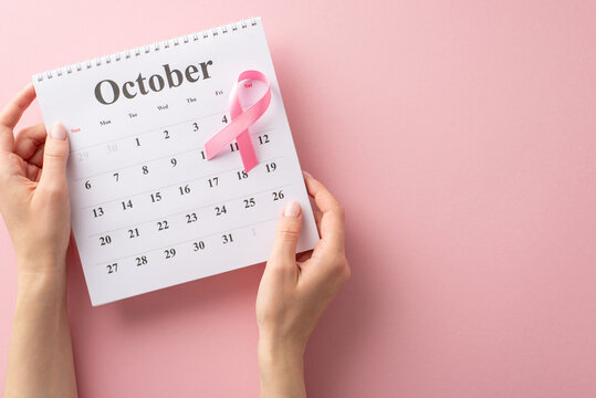 Commemorate International Breast Cancer Awareness Month with this top-view image of hands holding a calendar and pink ribbon on a pastel pink backdrop. Perfect for text or advertising placements