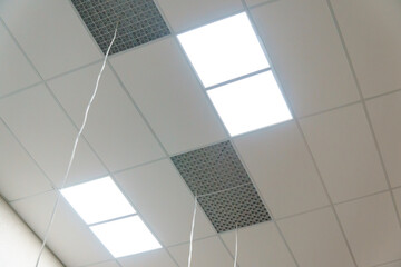 White suspended ceiling with square fluorescent lights in an office space. Design and details of a...