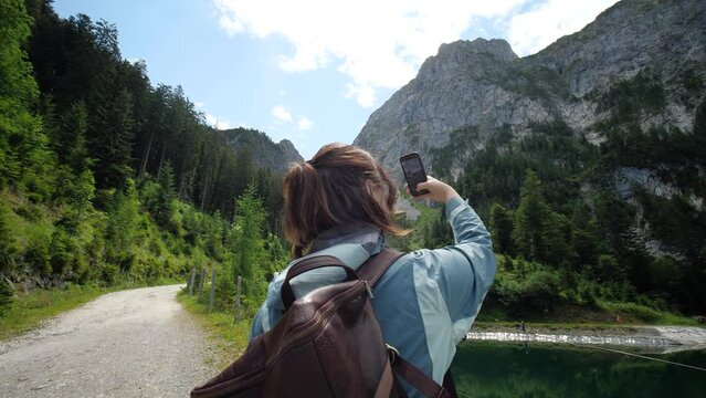 Female tourist in Alps taking pictures of mountains with a phone while hiking